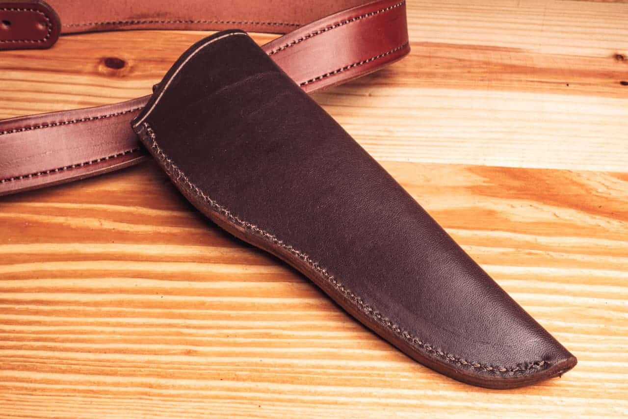 A handmade leather sheath sitting on top of a wooden table.