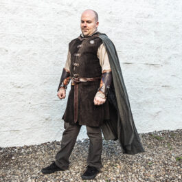 A man dressed in medieval clothing wearing Strider Vambraces standing in front of a white wall.