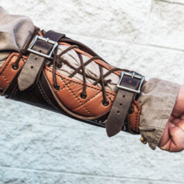 A person wearing Strider Vambraces holding onto a piece of leather.