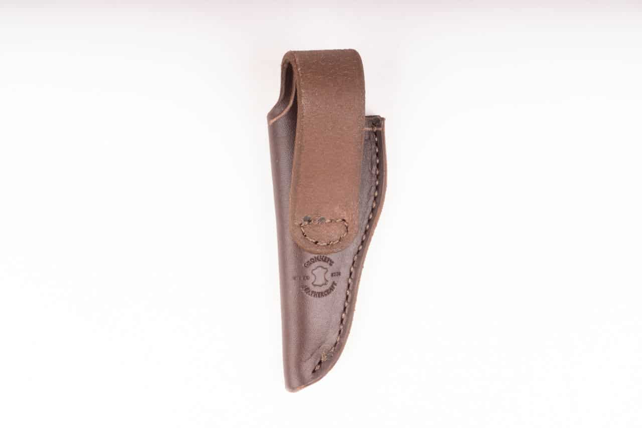 A brown handmade leather sheath hanging from a wall.