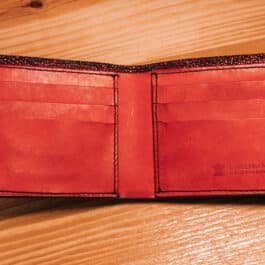 A metallic red rayskin wallet sitting on top of a wooden table.